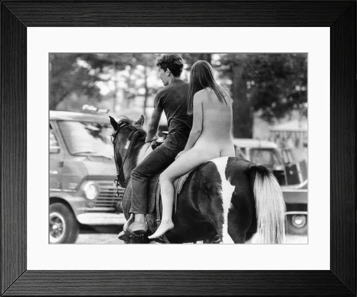 Framed Print : A naked young women and her escort ride a horse through Goose Lake Park during the site of the three day rock music festival