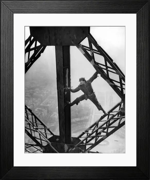 Framed Print : Worker painting the Eiffel Tower. Working without a safety harness he precariously straddles steel beams