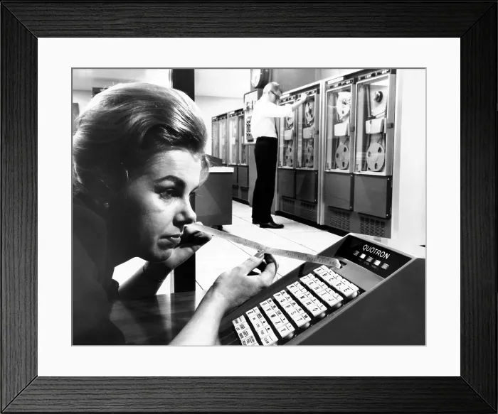 Framed Print : Woman holds tape with the latest stock prices printed by the Quotron II Framed Print : Woman holds tape with the latest stock prices printed by the Quotron II