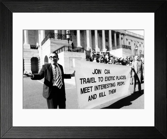 Framed Print : Rally protesting U.S. involvement in Angola. Demonstrators in front of the Capitol wear masks of Henry Kissinger and a pig. Their sign reads, Join CIA