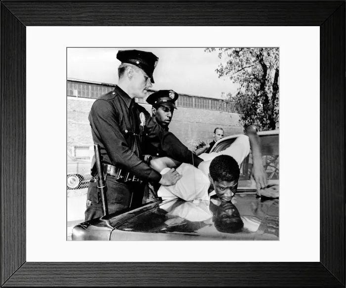 Framed Print : Violence in Los Angeles street. Police hold a African American teenager over the hood of a police car Framed Print : Violence in Los Angeles street. Police hold a African American teenager over the hood of a police car