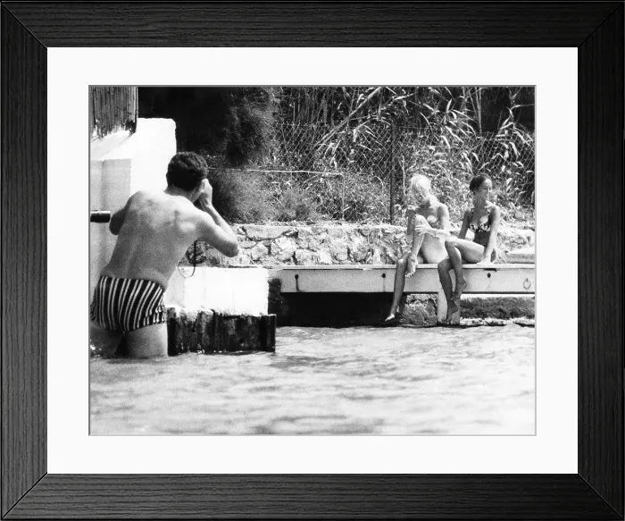 Framed Print : An intrusive photographer takes photos of Brigitte Bardot and her companion in St. Tropez, France. Her home on the shore was often approached from the water by paparazzi