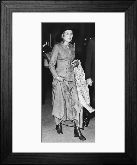 Framed Print : Singer Marianne Faithful at Heathrow Airport after arriving from Dublin, June 26, 1970. She wears a newly fashionable menswear suit with a maxi skirt and a snake skin coat