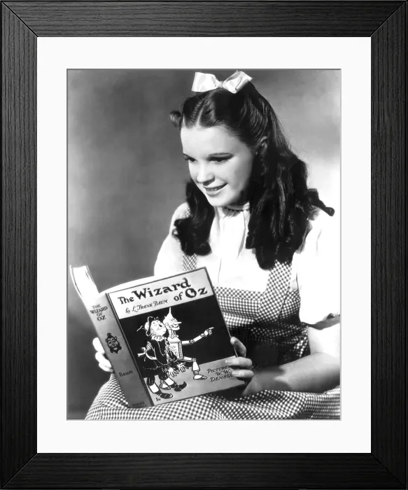 Framed Print : JUDY GARLAND, dressed as Dorothy reading The Wizard of Oz