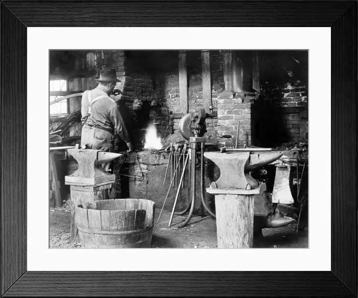 Framed Print : Occupational portrait of a blacksmith, in his smithy with anvils, ca. 1906