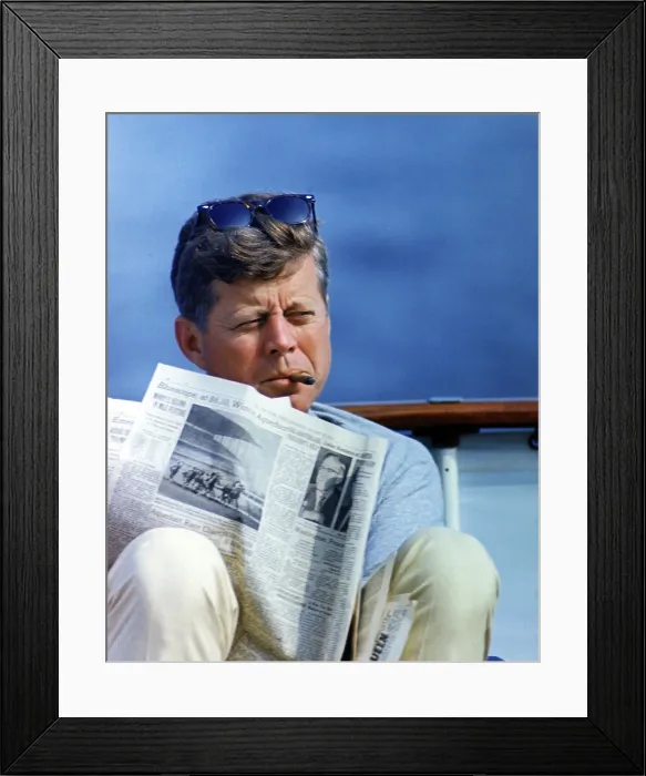 Framed Print : President John Kennedy smoking a cigar while reading the New York Times, aboard the family yacht, Honey Fitz in Hyannisport, Massachusetts. 1963