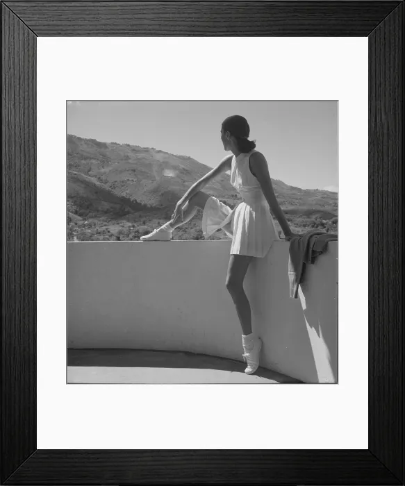Framed Print : Woman wearing tennis outfit, seated on wall, with one leg on top of wall, looking at the mountains behind her, photograph by Toni Frissell, 1947