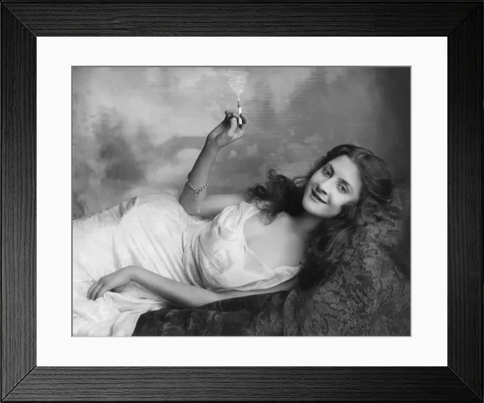 Framed Print : Young woman lying on a sofa and holding a burning cigarette, photograph by Fritz W. Guerin, 1902