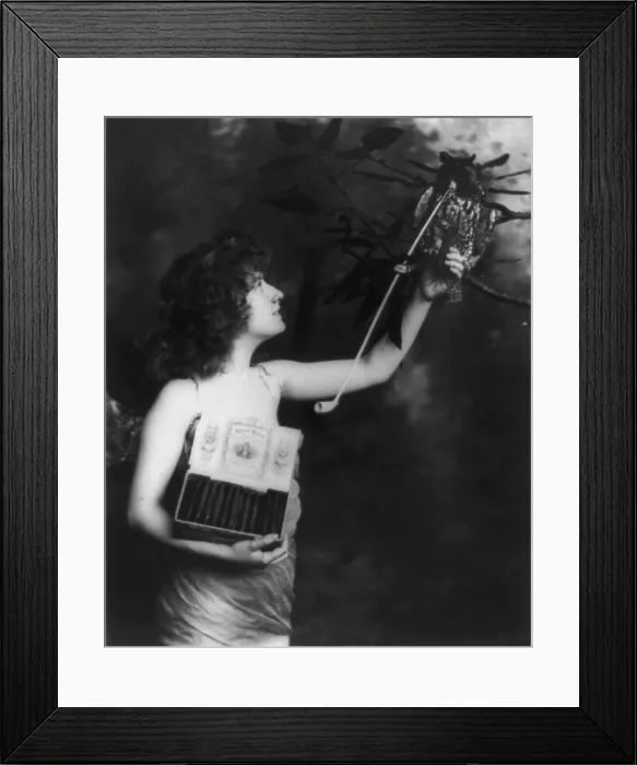 Framed Print : Woman wearing a winged costume and holding box of Robert Burns cigars, offering a cigar to a stuffed owl with long pipe in its mouth, original title: Have One