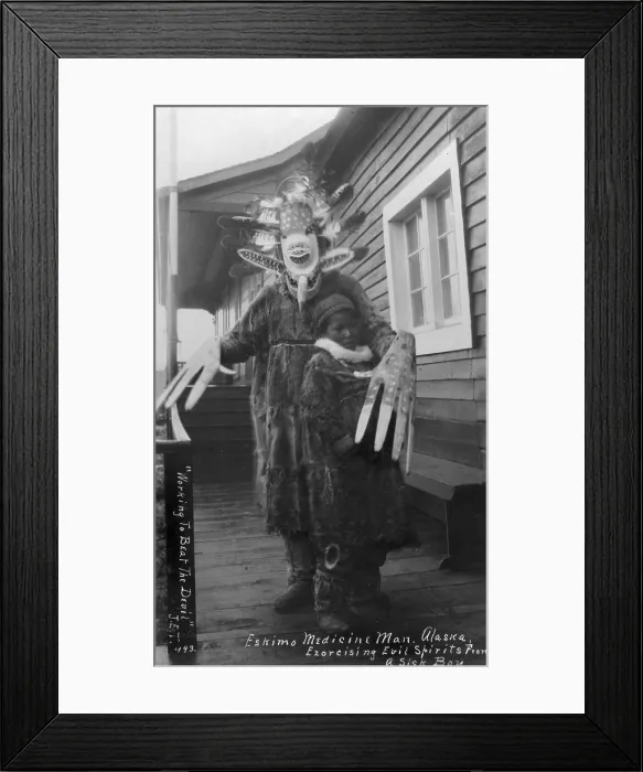 Framed Print : Eskimo medicine man in mask and sick boy, original title: Working to beat the devil, Eskimo medicine man exorcising evil spirits from a sick boy, circa 1900-1930