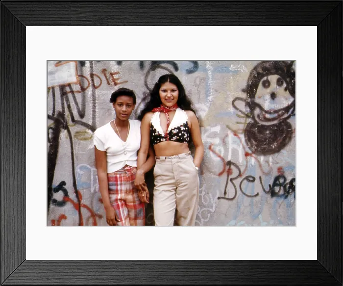 Framed Print : 1970s America. Two young girls pose in front of a graffitied wall in Brooklyn, New York City, ca. 1973