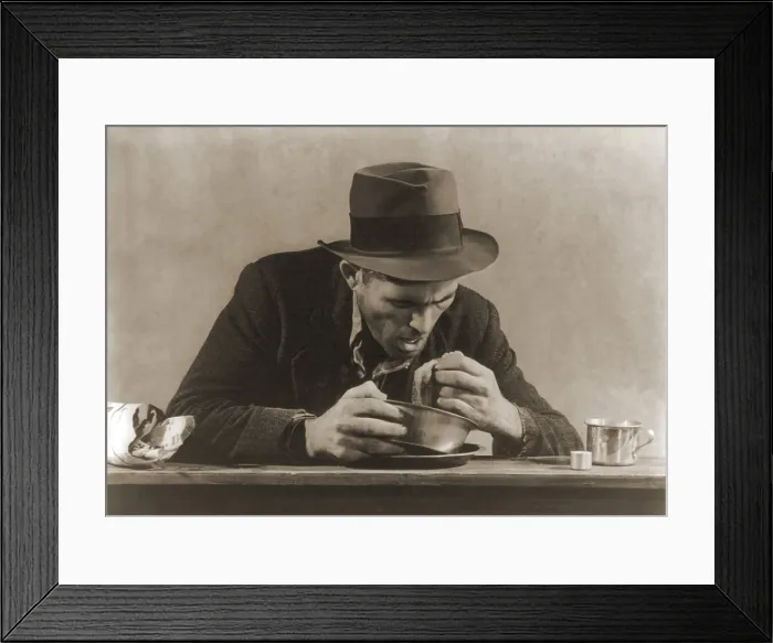 Framed Print : Hungry man with his meal of bread and soup at a New York City soup kitchen during the Great Depression. His fedora and now ragged sports jacket indicate his past employment. 1930s