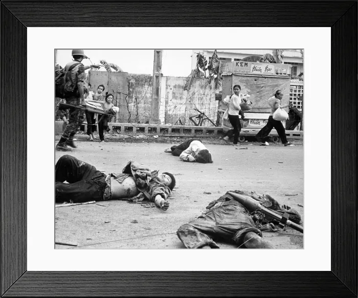 Framed Print : Vietnam War, women and children loaded down with salvage and possessions scurry past the bodies of three Viet Cong killed during the fighting, circa late 1960s
