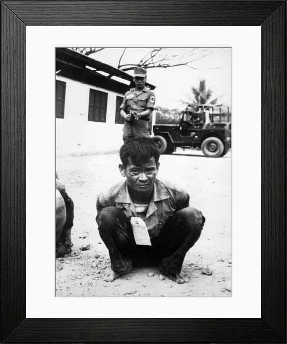 Framed Print : Vietnam War, Viet Cong, heavily guarded, awaits interrogation following capture in the attacks on the capital city during the festive Tet holiday period, circa late 1960s