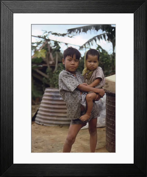 Framed Print : Vietnam War, Camp Campbell, Phu Bai, Republic of Vietnam. A Vietnamese boy carries a young child, circa late 1960s