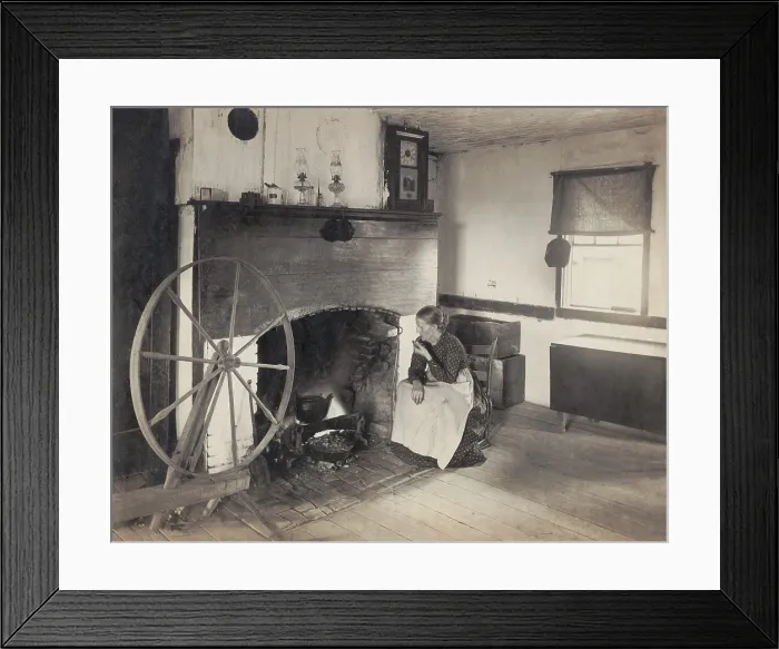 Framed Print : OLDEN TIMES. Middle aged woman watching her cooking from a rocking chair by a fireplace as she smokes a pipe