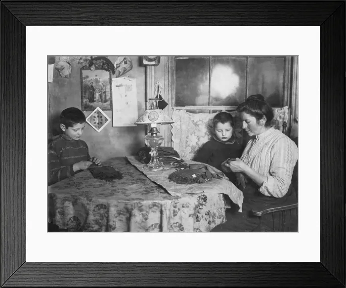 Framed Print : Late at night, sewing tapes on gloves. The boy helps. Family of five sleep in room where the work is done, New York, photograph by Lewis Wickes Hine, February 1908