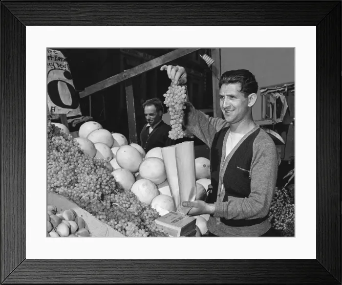 Framed Print : New York City, Pushcart vendor bagging grapes at his produce stand, photograph, 1940