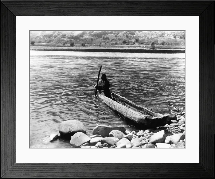 Framed Print : Nez Perc canoe. Nez Perc man with pole maneuvering dugout canoe to rocky shore. Edward S. Curtis, ca. 1910