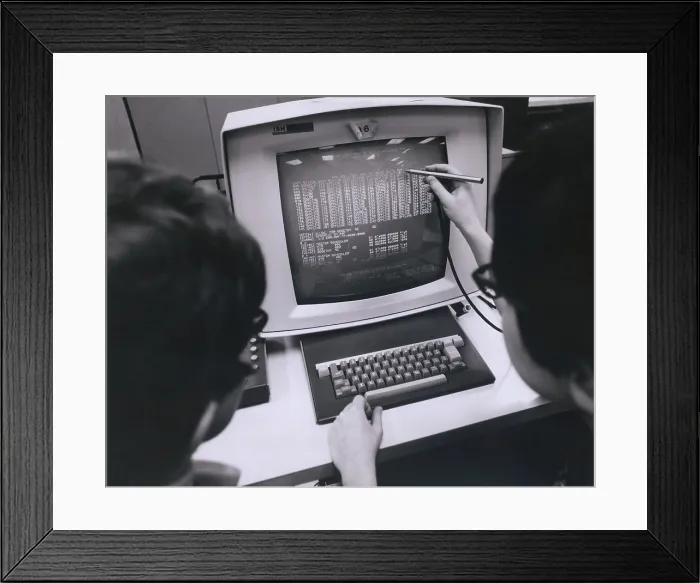 Framed Print : IBM programmers work at a cathode ray monitor with a touch-screen pointer. Ca. 1980 Framed Print : IBM programmers work at a cathode ray monitor with a touch-screen pointer. Ca. 1980