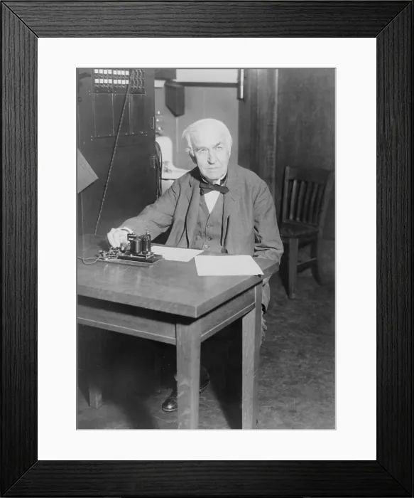 Framed Print : Thomas Edison, seated at desk, demonstrating an old telegraph transmitter in his West Orange, New Jersey, laboratory, 1930