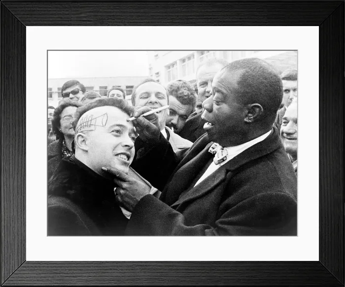 Framed Print : Louis Armstrong (1901-1971), African American Jazz musician, drawing a trumpet and autographing the side of a young man's head in Nice, France. 1960