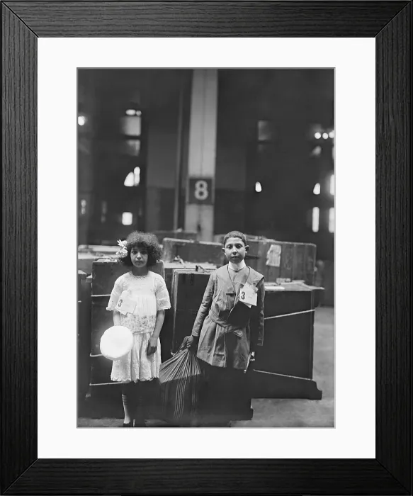 Framed Print : Two well dressed immigrant children tagged with ERIE labeled at Ellis Inland, in front of many steamer trunks. Ca. 1910 Framed Print : Two well dressed immigrant children tagged with ERIE labeled at Ellis Inland, in front of many steamer trunks. Ca. 1910