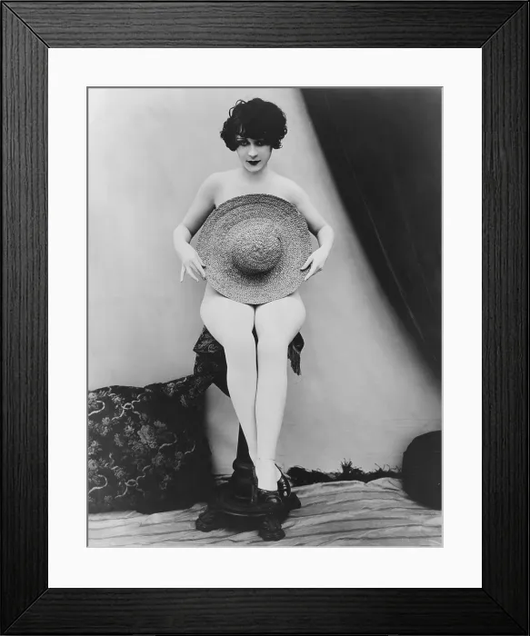 Framed Print : Studio portrait titled MISS MODESTY, showing a young woman posed to appear nude behind a large straw hat. 1926