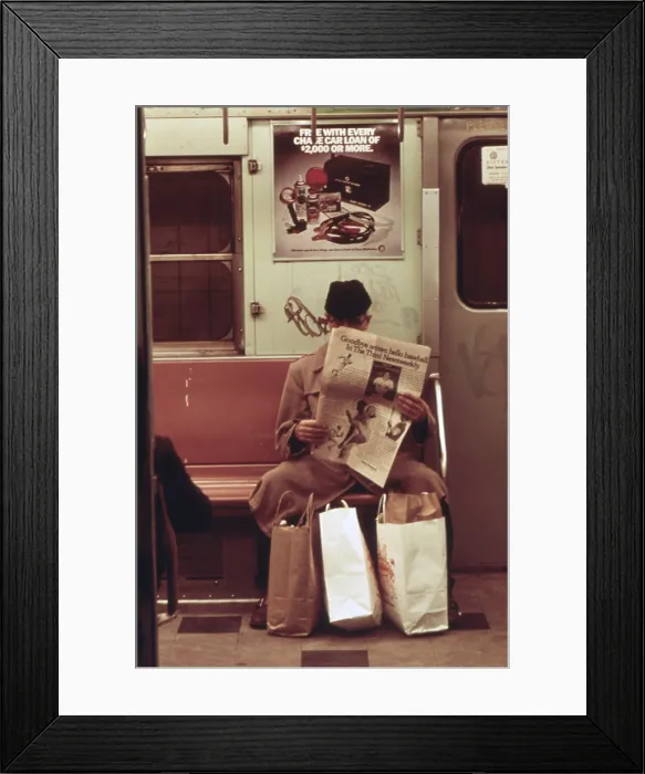 Framed Print : New York City Subway. A passenger is in his own world reading his newspaper with his shopping bags secured between his feet. May 1973