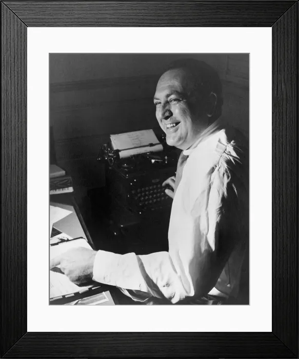 Framed Print : Film producer Val Lewton (1904-1951), working at his desk, with one hand on a script and the other on a typewriter. Ca. 1945