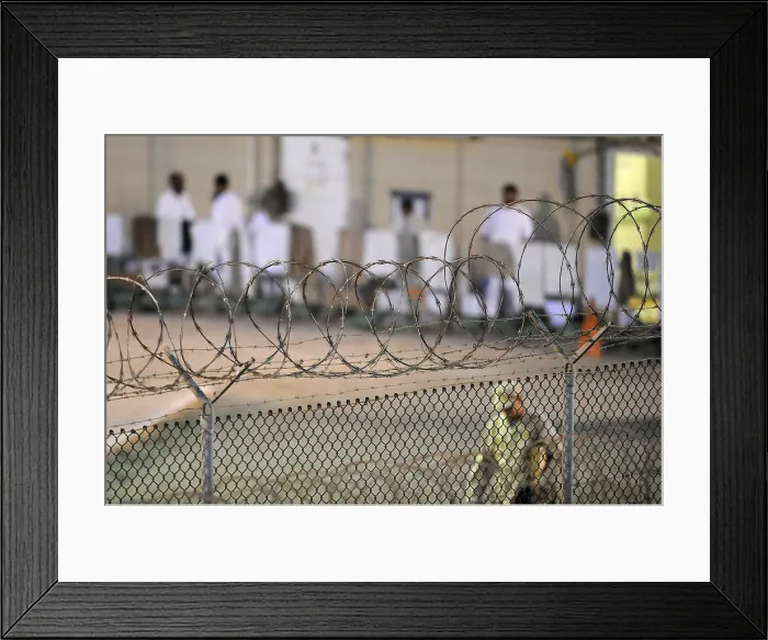 Framed Print : A U.S. Sailor foreground conducts an early morning patrol while detainees dressed in white background at a recreation yard inside Camp Delta at Guantanamo Bay Naval Base Cuba Framed Print : A U.S. Sailor foreground conducts an early morning patrol while detainees dressed in white background at a recreation yard inside Camp Delta at Guantanamo Bay Naval Base Cuba