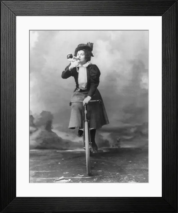 Framed Print : Madge Lessing (1866-1932), English actress and singer, riding bicycle, and holding musical horn to lips. 1898