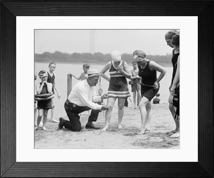 Framed Print : A beach official checks the amount of thigh exposed by a young ladies bathing suit in 1922. The hemlines on all women's clothing reached new heights in the 1920's