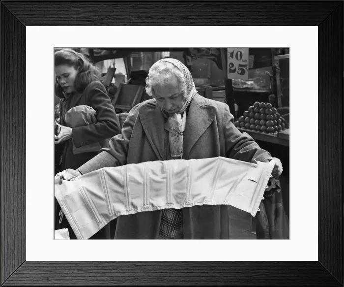 Framed Print : Elderly woman evaluating a corset at a pushcart market on Belmont Avenue, Brooklyn, New York. 1958