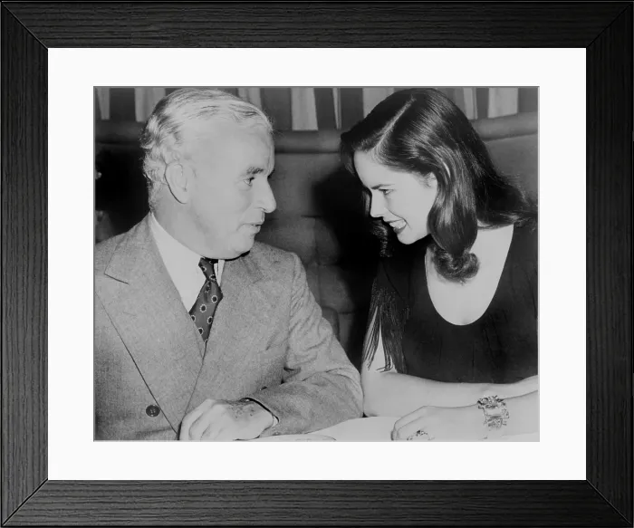 Framed Print : Charlie Chaplin (1889-1977) sitting with his young wife Oona at Hollywood nightclub in 1944. The couple married the previous year, when Oona was 18 and Charlie was 54
