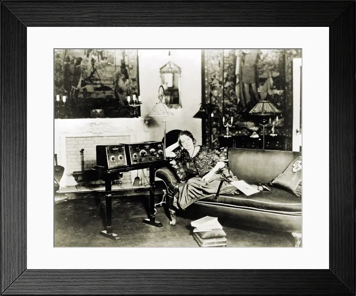 Framed Print : Broadcast radio's first decade prompted novel uses. Photo shows a shut-in woman, wearing radio headset, listening to radio on stand next to sofa. 1923