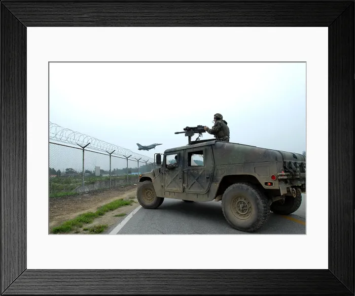 Framed Print : US Airman guards the base perimeter from the gun turret of a Humvee while an F-16 Fighter aircraft lands in the background. At Osan Air Base South Korea. July 23 2008