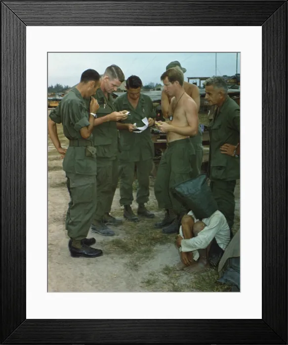 Framed Print : Vietnam War. A suspected Viet Cong sits on the ground with a black bag over his head while several US soldiers examine papers Framed Print : Vietnam War. A suspected Viet Cong sits on the ground with a black bag over his head while several US soldiers examine papers
