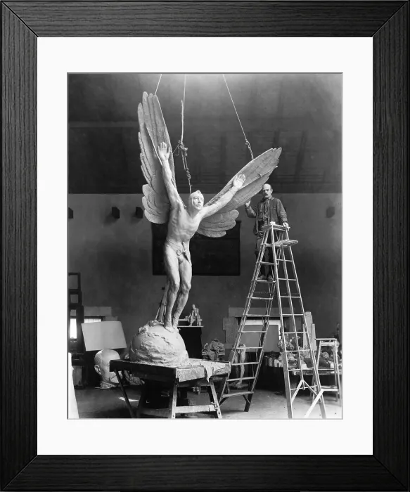 Framed Print : Sculptor Gutzon Borglum (1871-1941), standing on ladder, alongside his sculpture, STATUE OF AN AVIATOR, a memorial for James R. McConnell who was killed in World War I. 1919