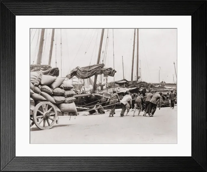 Framed Print : Gang of five Chinese dock workers lean hard on ropes to haul a heavy wagon load of sacks on the Hong Kong waterfront. Between 1890 and 1923