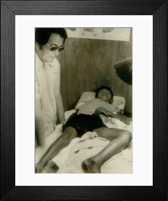 Framed Print : Jim Jones standing over a Guyanese boy with a near-fatal snake bite. He was in the Jonestown clinic and then airlifted to Georgetown. People's Temple Agricultural Project