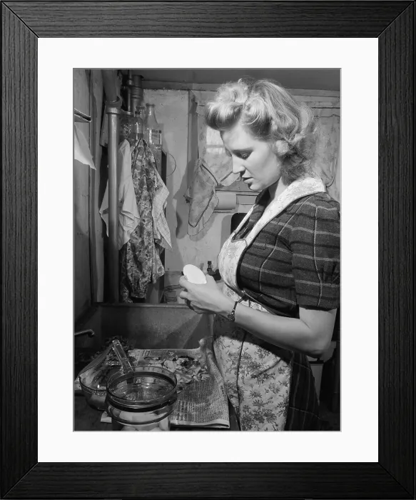 Framed Print : Young women peeling potatoes in her Washington D.C. apartment kitchen. She has a modern glass cooking pot and uses a newspaper to collect the potato peels for the garbage. Dec