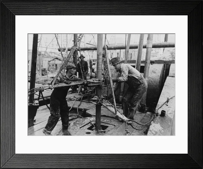 Framed Print : Oil roughnecks screw one piece of drill pipe to another piece with a heavy pipe wrench. In the mid 20th century Texas was a major oil producing region for the United States