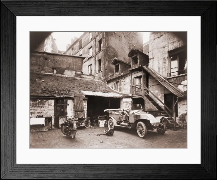 Framed Print : Automobile and two motorcycles in courtyard on Rue de Valence, Paris, photographed by Eugene Atget with a large-format wooden bellows camera. Ca. 1920