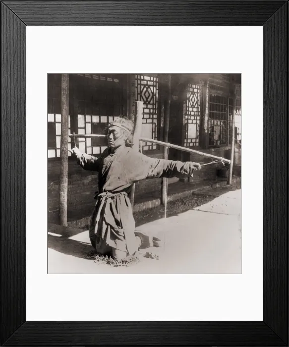 Framed Print : Chinese prisoner kneeling on chains, with his ankles in stocks, while his arms are tied by the thumbs to a pole supporting his arms. Moukden, China. Circa. 1900 Framed Print : Chinese prisoner kneeling on chains, with his ankles in stocks, while his arms are tied by the thumbs to a pole supporting his arms. Moukden, China. Circa. 1900