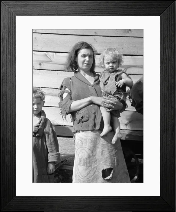 Framed Print : Young mother dressed in a ragged sweater and a skirt made of flour sacks holds her toddler. She lives with eight others in a field on U.S