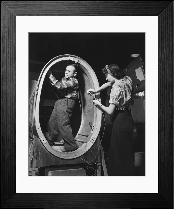 Framed Print : A small man installs control wires inside the fuselage of a Valiant basic trainer while a woman works standing outside. Vultee Aircraft Downey Plant California. Ca