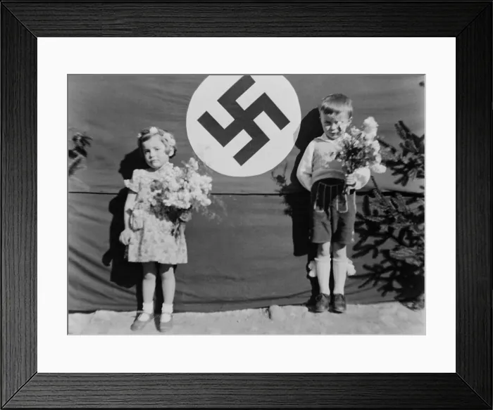 Framed Print : Young German girl and boy at a Nazi ceremony, ca. 1937. They hold flowers and stand beside a large swastika, in Muhldorf am Inn, Germany. (BSLOC_2013_11_28) Framed Print : Young German girl and boy at a Nazi ceremony, ca. 1937. They hold flowers and stand beside a large swastika, in Muhldorf am Inn, Germany. (BSLOC_2013_11_28)