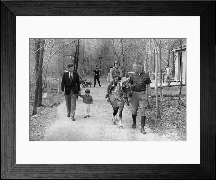 Framed Print : Kennedy family weekend at Camp David. President Kennedy, walks with his 2 year old son John Jr. and Caroline Kennedy rides a pony named Tex