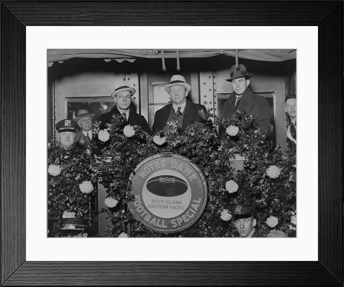 Framed Print : Knute Rockne standing on rear of train car decorated with flowers, 1930. Rockne is flanked by Coach Frank Cariedo and football player Tom Conley as they leave for California